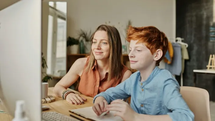 Boy with woman tutor, smiling while looking at a computer